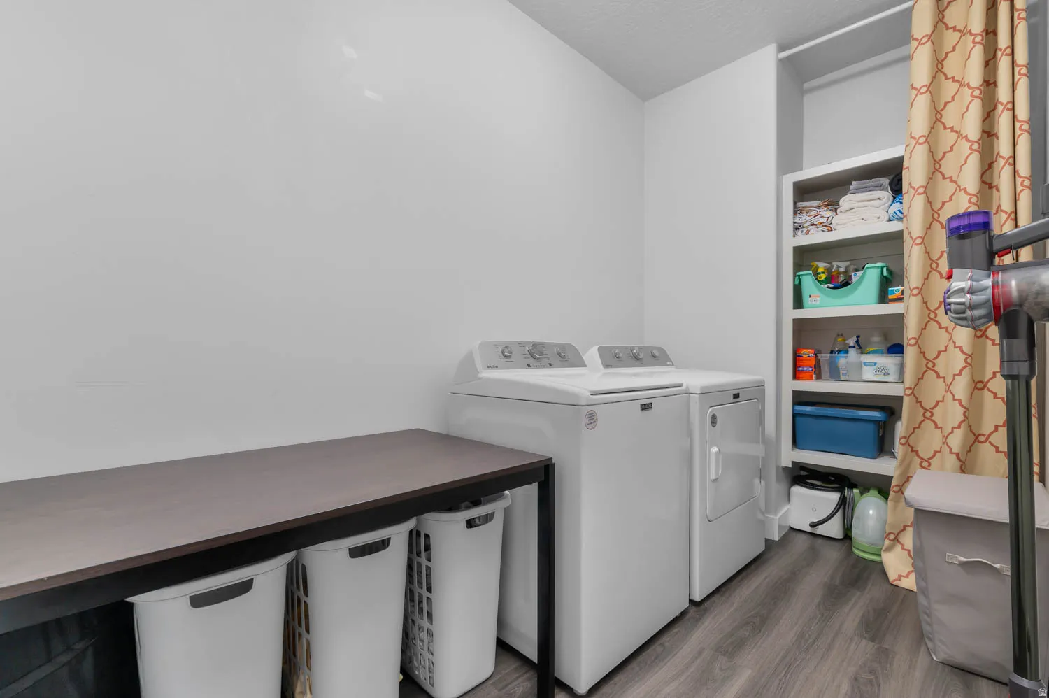 Dedicated laundry area featuring a washer and dryer, wood-finish flooring, built-in shelving, and a dark countertop workspace