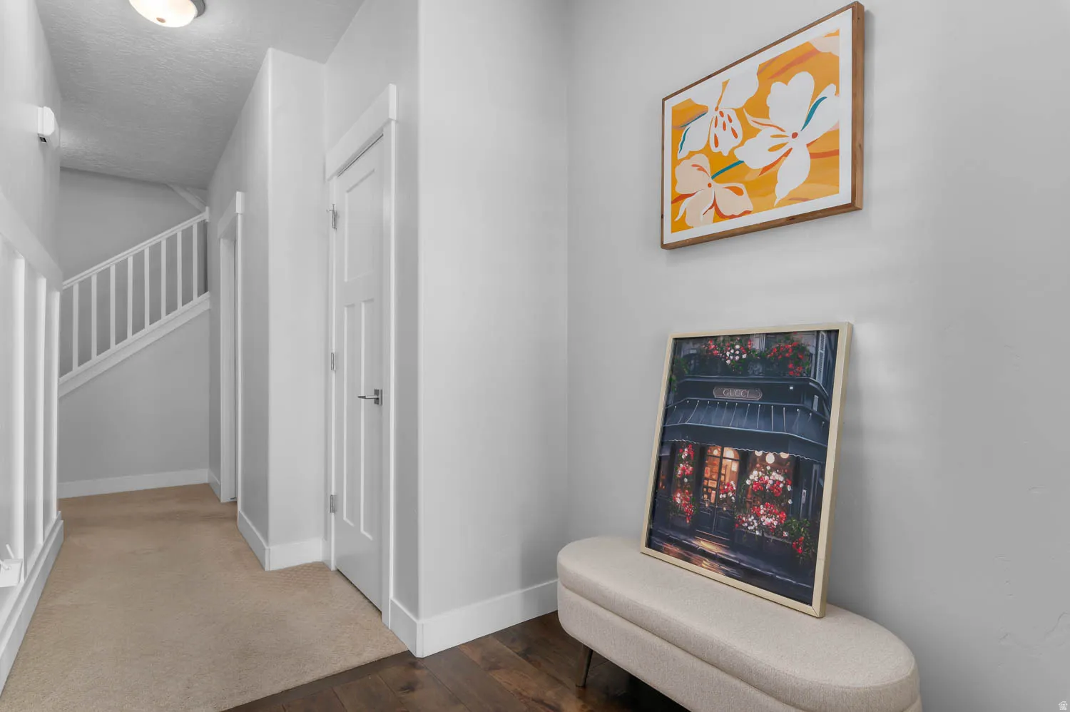 Hallway featuring wood-finish flooring, light tan carpeting, white interior doors with contemporary hardware, white baseboards, and a staircase with white balusters