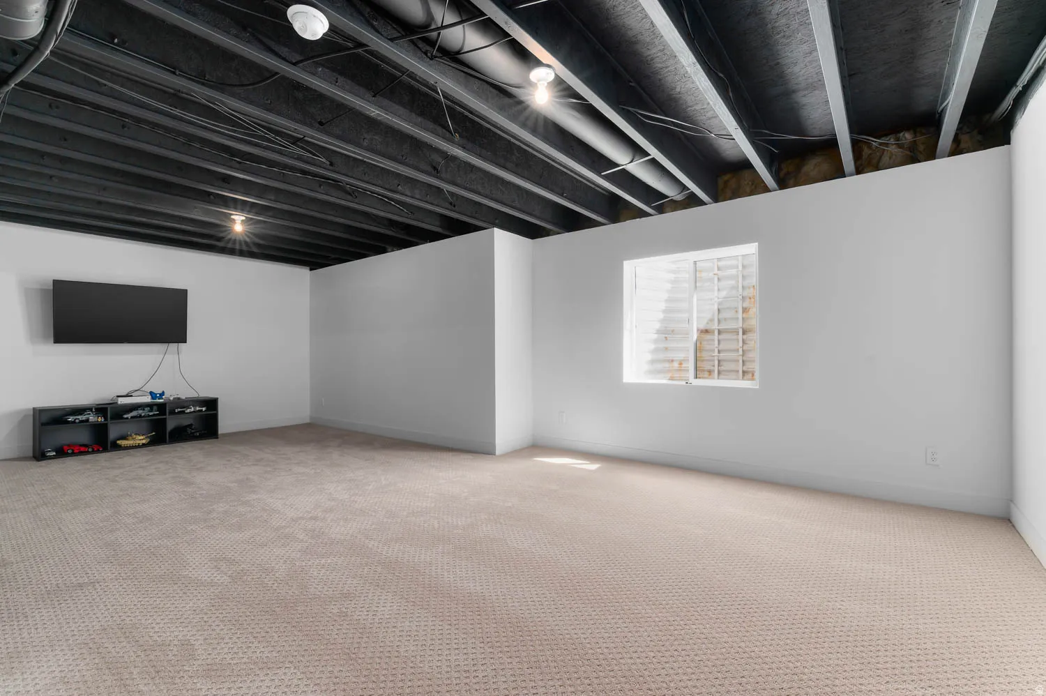 Spacious room featuring light-colored patterned carpeting, white painted walls, and an exposed black painted ceiling with recessed lighting