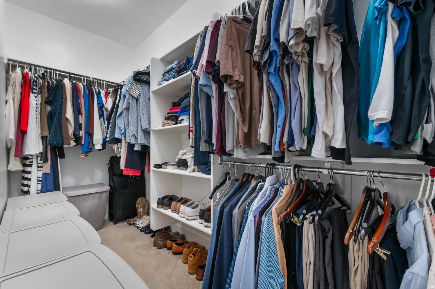 Walk-in closet featuring white built-in shelving, multiple hanging rods, and carpet flooring