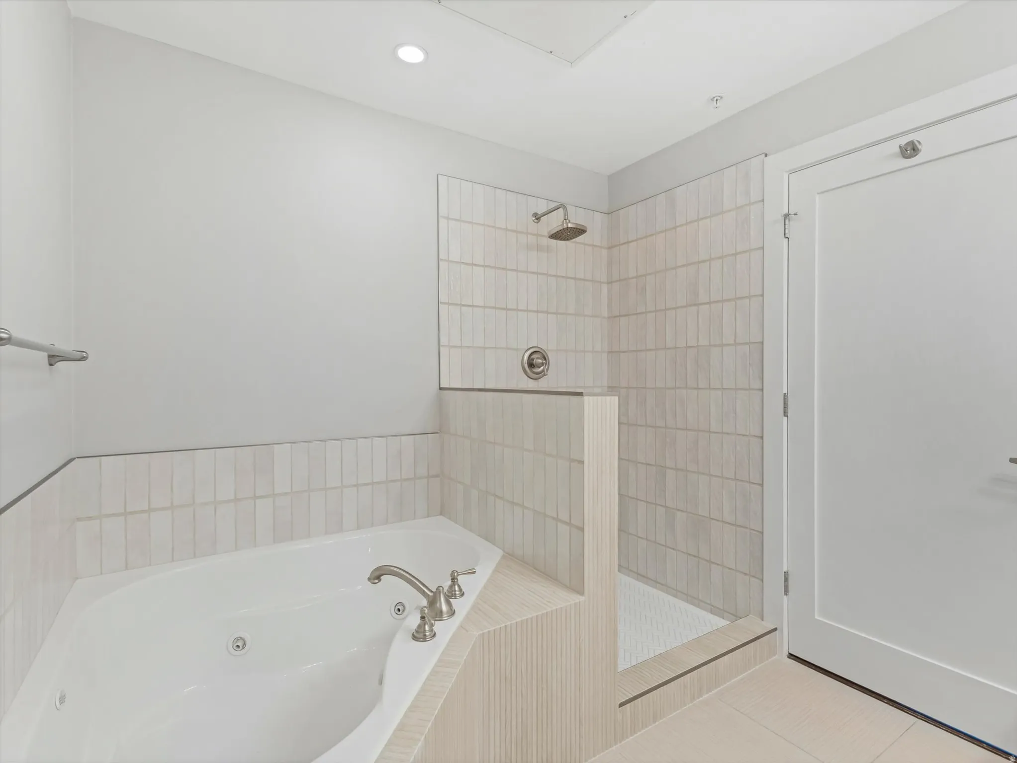 Bathroom featuring a jetted tub, a walk-in shower with a rain showerhead, light-colored vertical tile, and coordinating floor tile