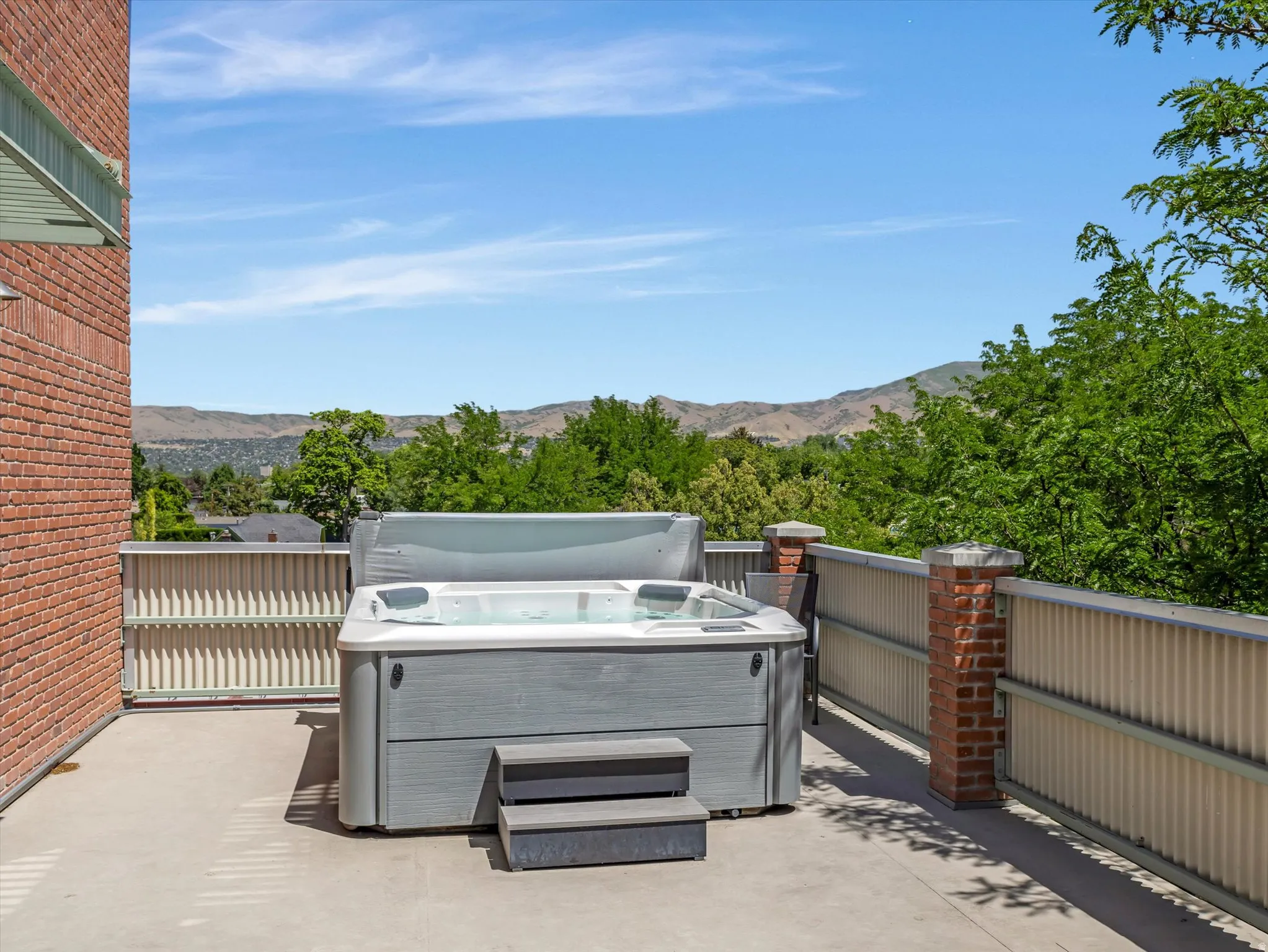 Outdoor deck featuring a built-in hot tub with steps, concrete flooring, and a brick exterior wall
