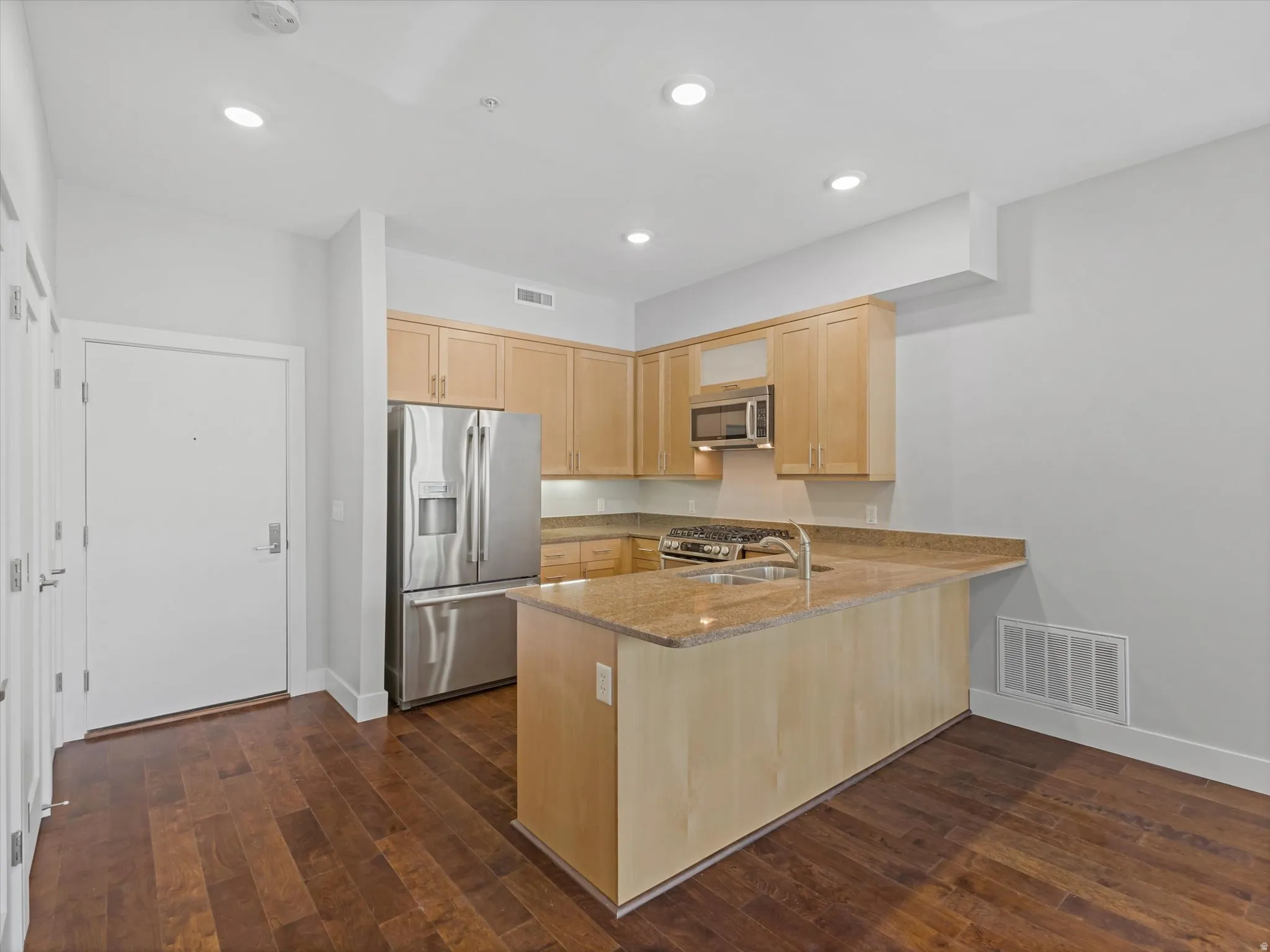 Kitchen featuring wood-finish flooring, light wood cabinetry, stainless steel appliances, and a central island with a sink