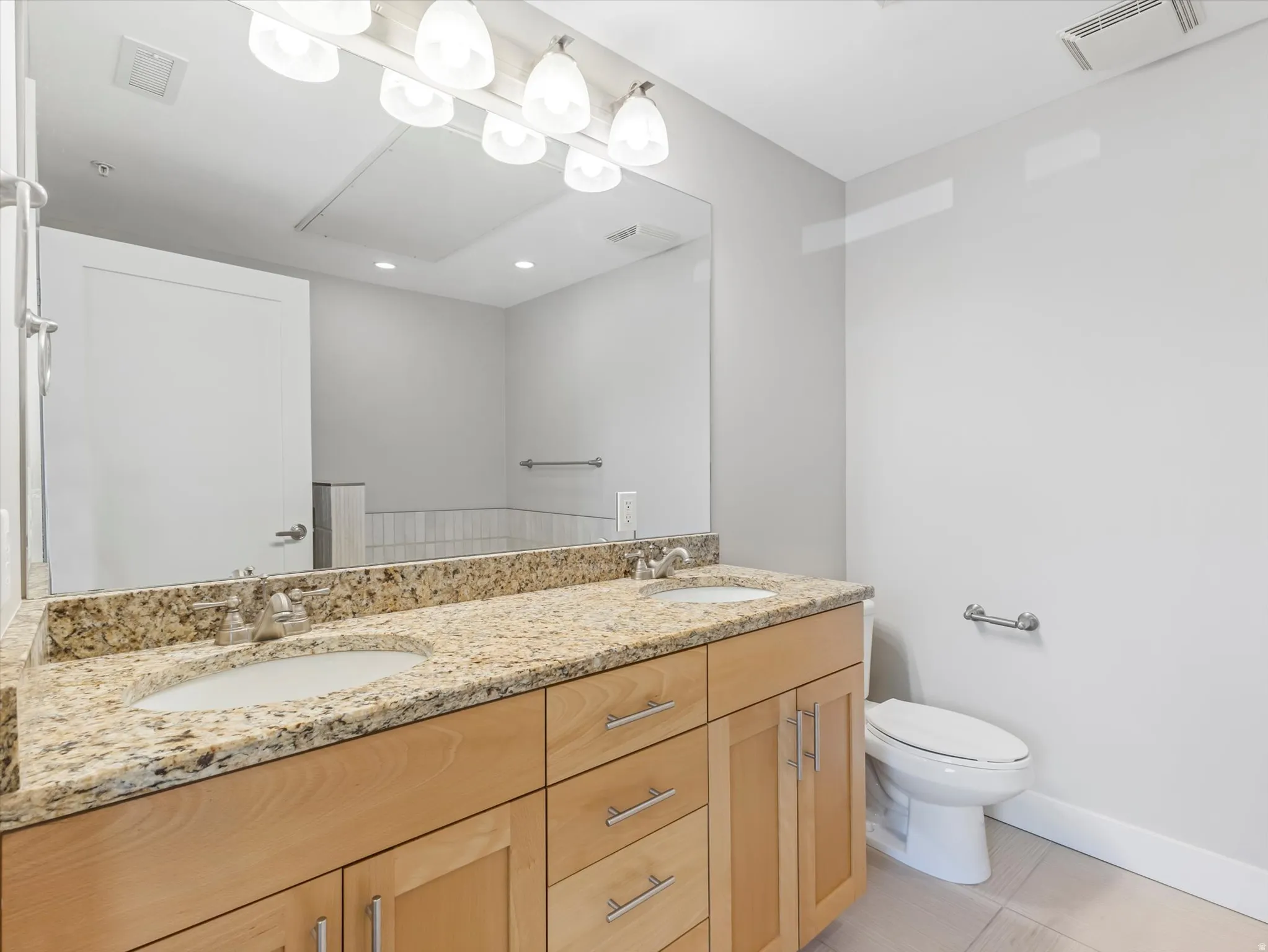 Double vanity featuring undermount sinks, granite countertops, and light wood cabinetry with brushed nickel hardware