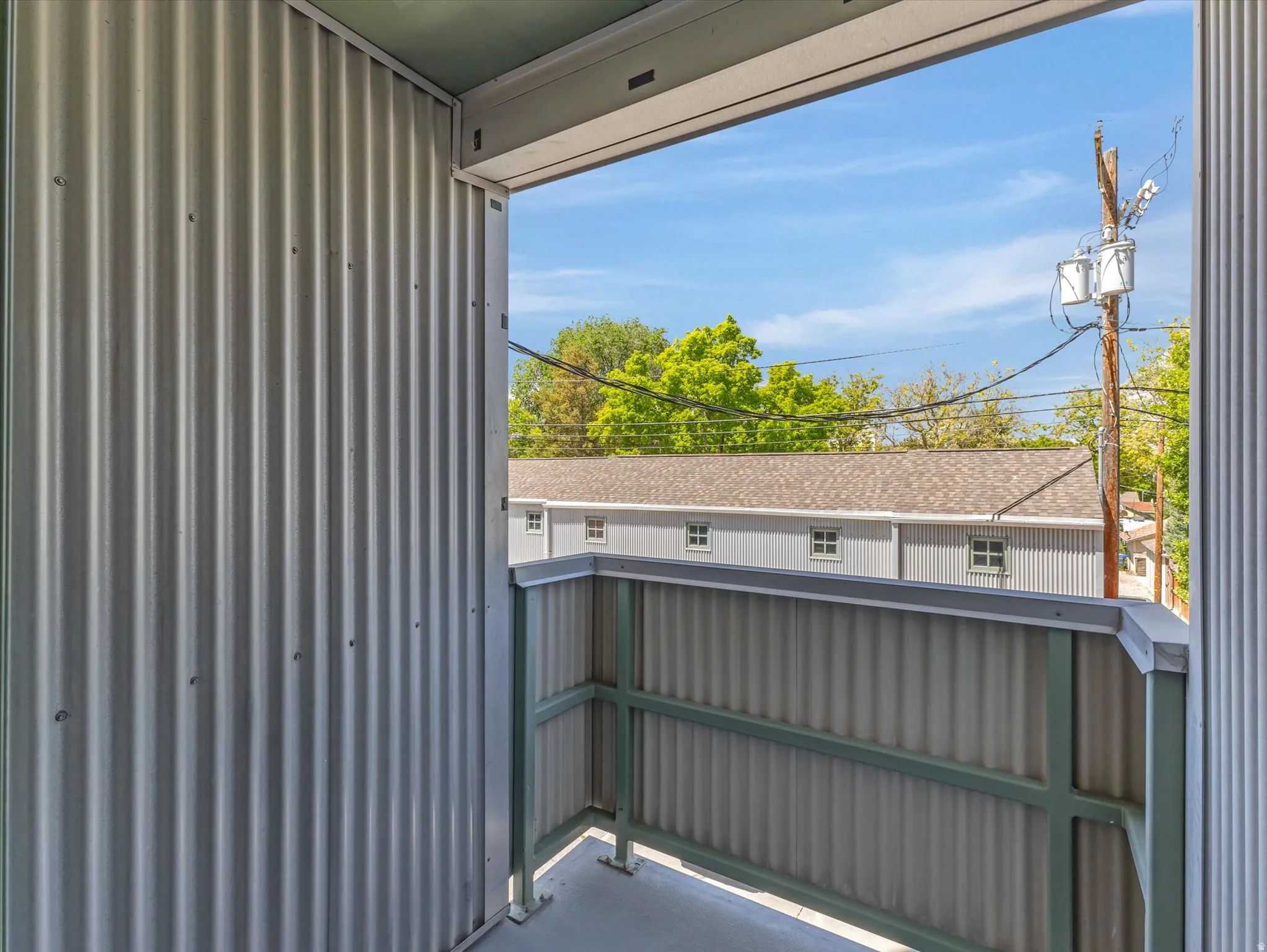 Private balcony with corrugated metal siding, green trim, and a concrete floor