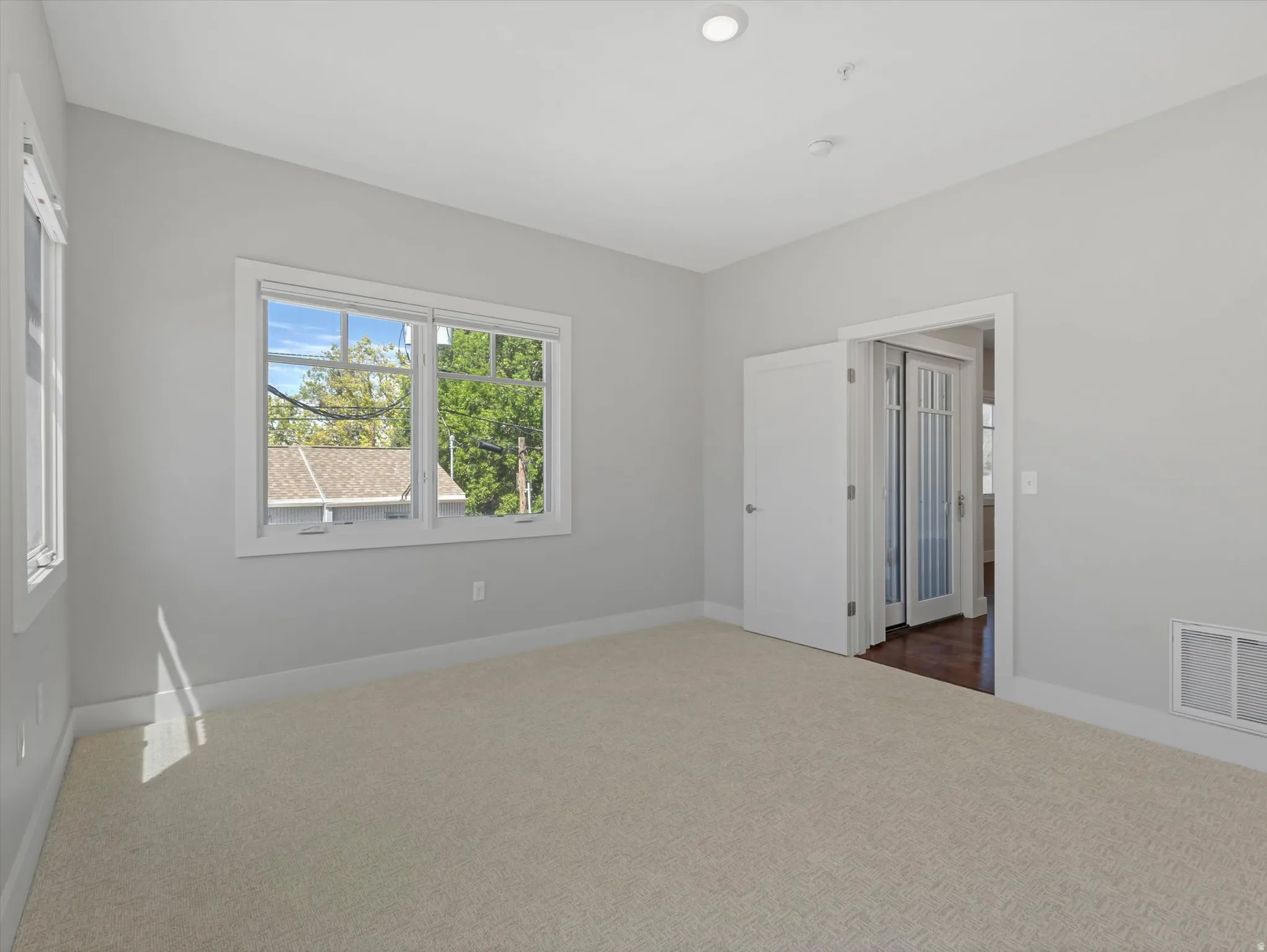 Carpeted interior space featuring white trim, multiple windows, recessed lighting, and a doorway with French doors