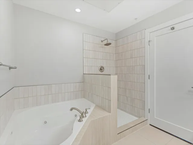 Bathroom featuring a jetted tub, a walk-in shower with a rain showerhead, light-colored vertical tile, and coordinating floor tile