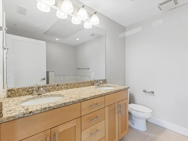 Double vanity featuring undermount sinks, granite countertops, and light wood cabinetry with brushed nickel hardware