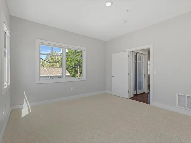 Carpeted interior space featuring white trim, multiple windows, recessed lighting, and a doorway with French doors
