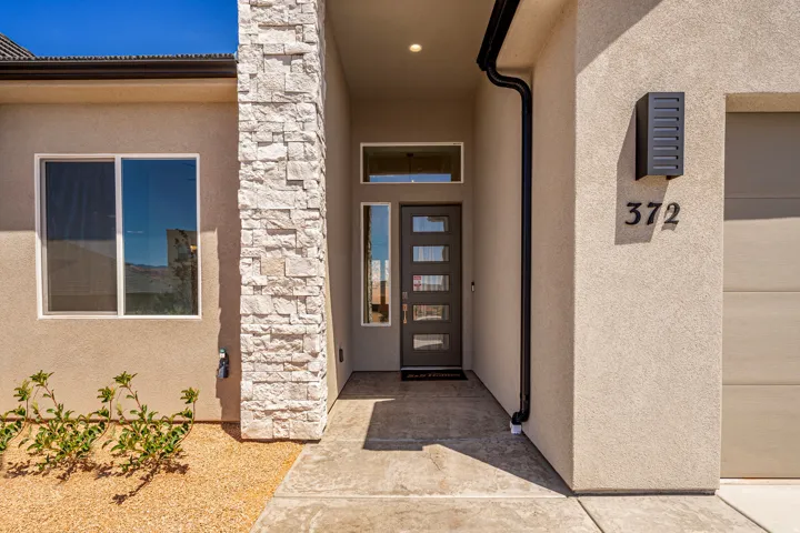 Modern exterior entry featuring stacked stone accents, stucco siding, a contemporary front door with multiple glass panes, and an integrated outdoor sconce