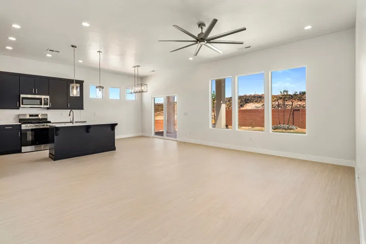 Open-concept living area featuring light wood-finish flooring, a modern ceiling fan, and large windows