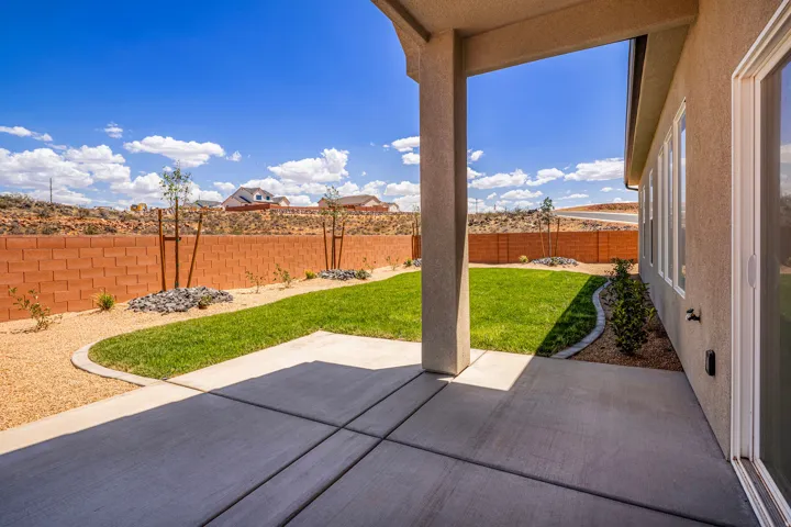 Covered concrete patio with segmented flooring, leading to a manicured lawn area