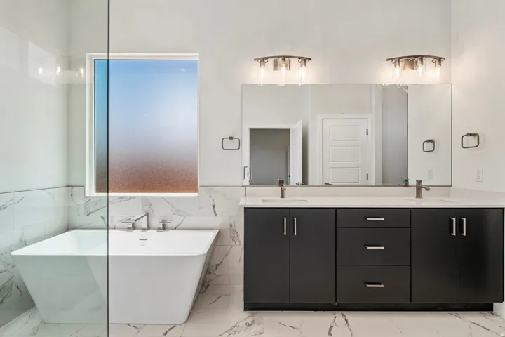 Contemporary bathroom featuring a freestanding soaking tub, a dual vanity with dark cabinetry, integrated rectangular sinks, and a large wall-mounted mirror