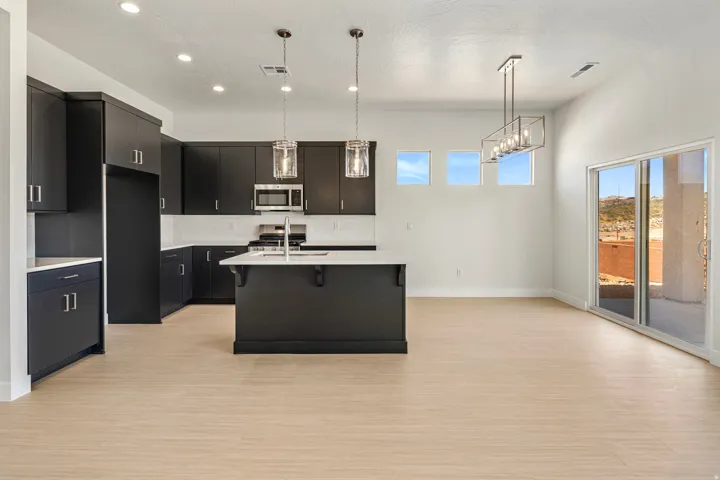 Open-concept kitchen and dining area featuring dark cabinetry with brushed nickel hardware, white countertops, wood-finish flooring, and a sliding glass door to exterior