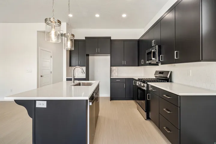 Modern kitchen featuring dark cabinetry, light countertops, stainless steel appliances, and a white hexagonal tile backsplash