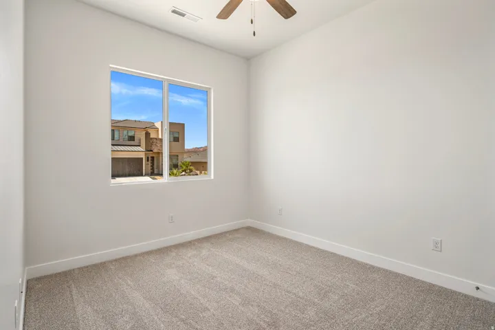 Neutral carpeted room with a large window, white walls, and a ceiling fan