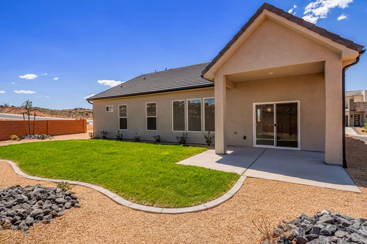 Rear exterior featuring a covered patio with concrete flooring, sliding glass door, and a gravel and grass landscaping design