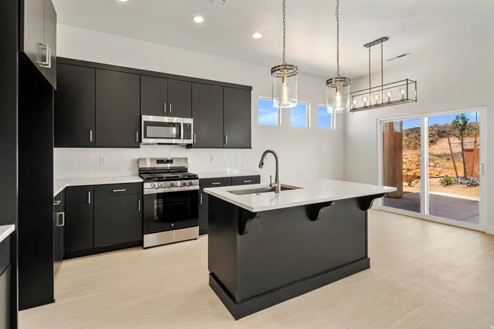 Modern kitchen featuring dark cabinetry, stainless steel appliances, a white subway tile backsplash, and a central island with an integrated sink and gooseneck faucet