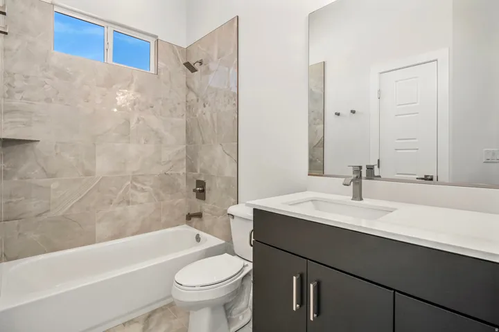 Bathroom featuring a soaking tub with stone-finish tile surround, a built-in shower niche, a window, a dark wood-finish vanity with an integrated sink, and a large wall-mounted mirror