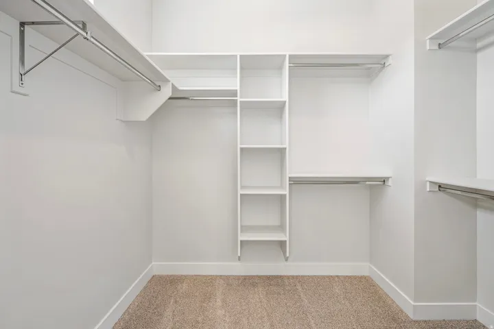 Walk-in closet featuring built-in shelving, multiple hanging rods, and neutral-toned carpeting