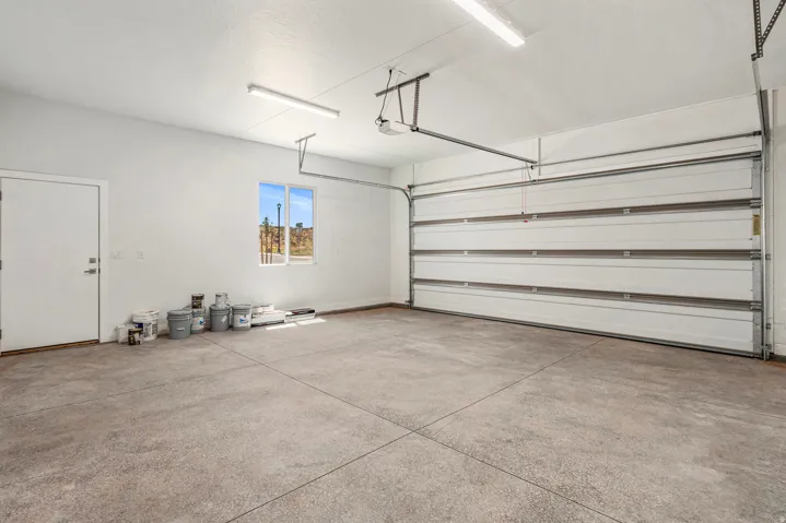 Spacious garage featuring a concrete floor, overhead lighting, a window, and an interior access door