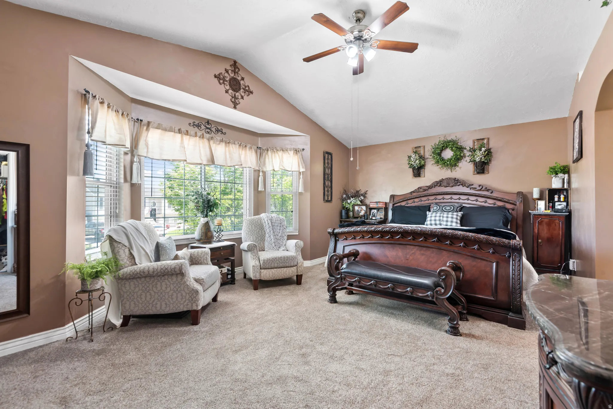 Vaulted ceiling room featuring a bay window, carpet flooring, a ceiling fan with integrated lighting, a built-in archway, and a built-in vanity with a stone-finish countertop