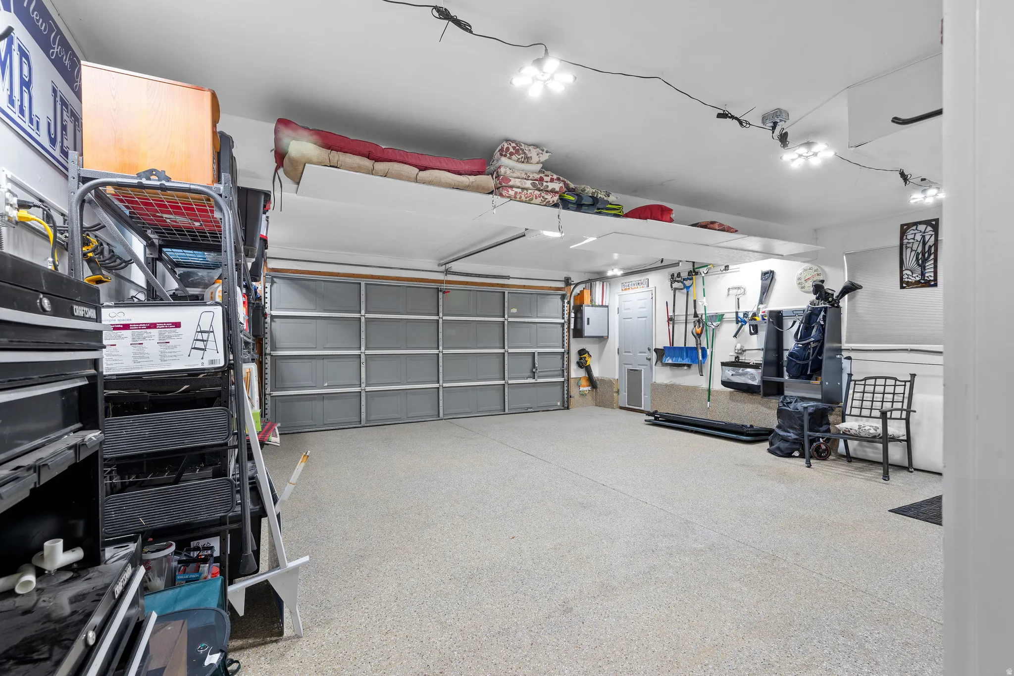 Spacious garage featuring a large overhead door, speckled epoxy flooring, overhead track lighting, and a substantial overhead storage shelf
