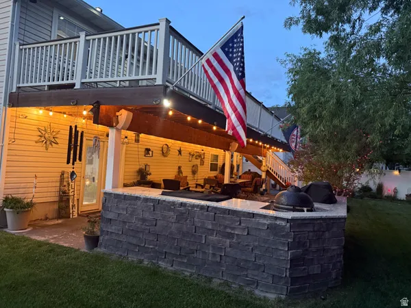 Outdoor entertaining area featuring a stone-clad kitchen island with a built-in grill, granite countertop, and string lighting under a covered patio