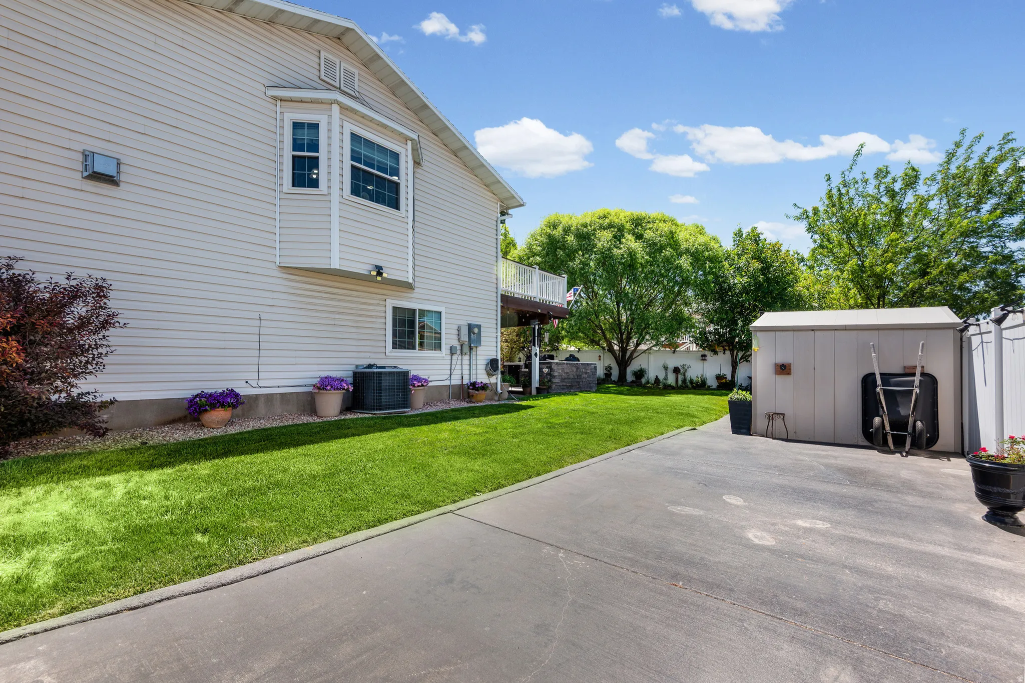 Expansive paved driveway alongside a manicured lawn, featuring a bay window, a storage shed, and a privacy fence