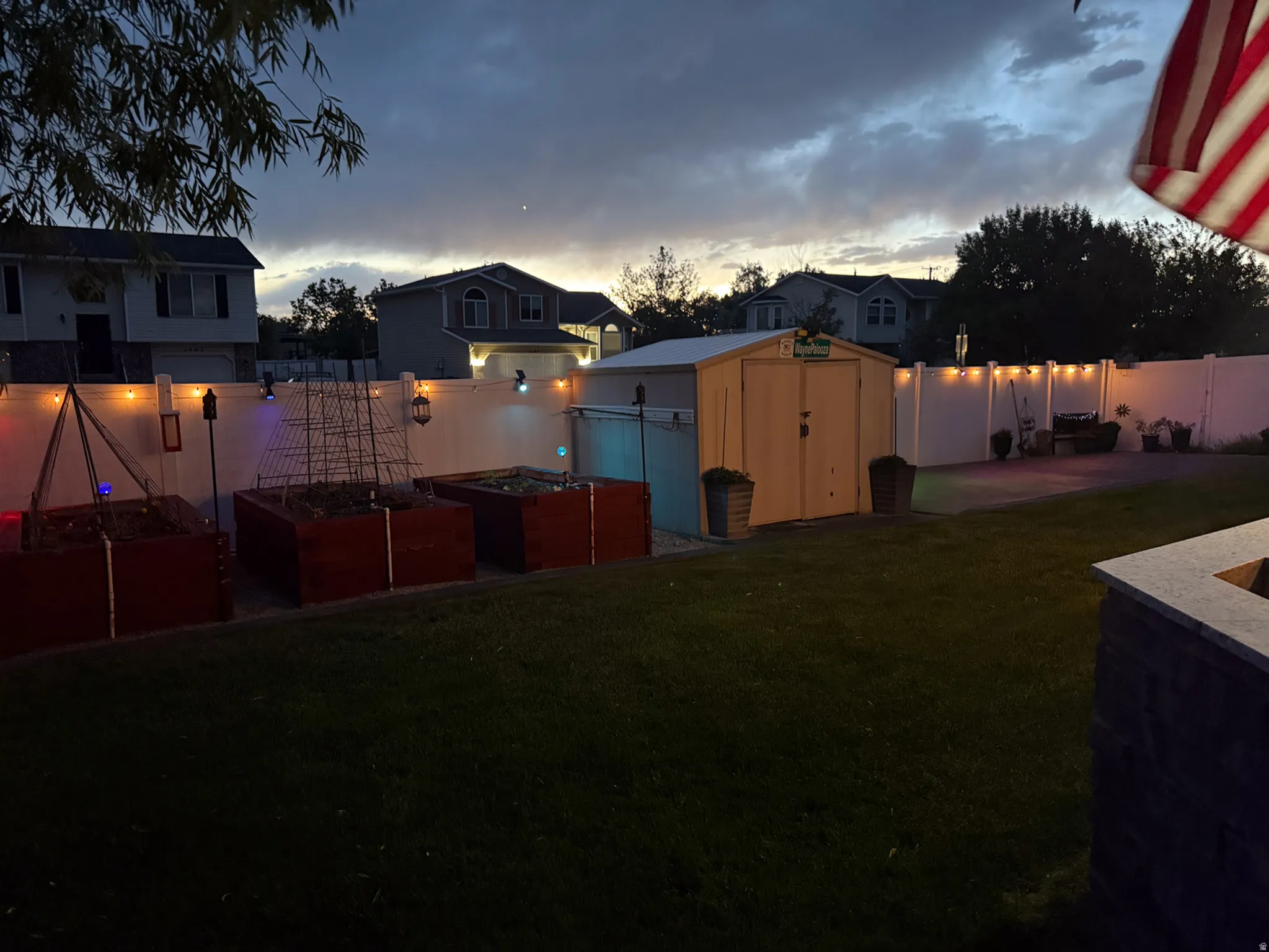 Expansive backyard featuring a manicured lawn, white vinyl fencing, a metal storage shed, and raised garden beds