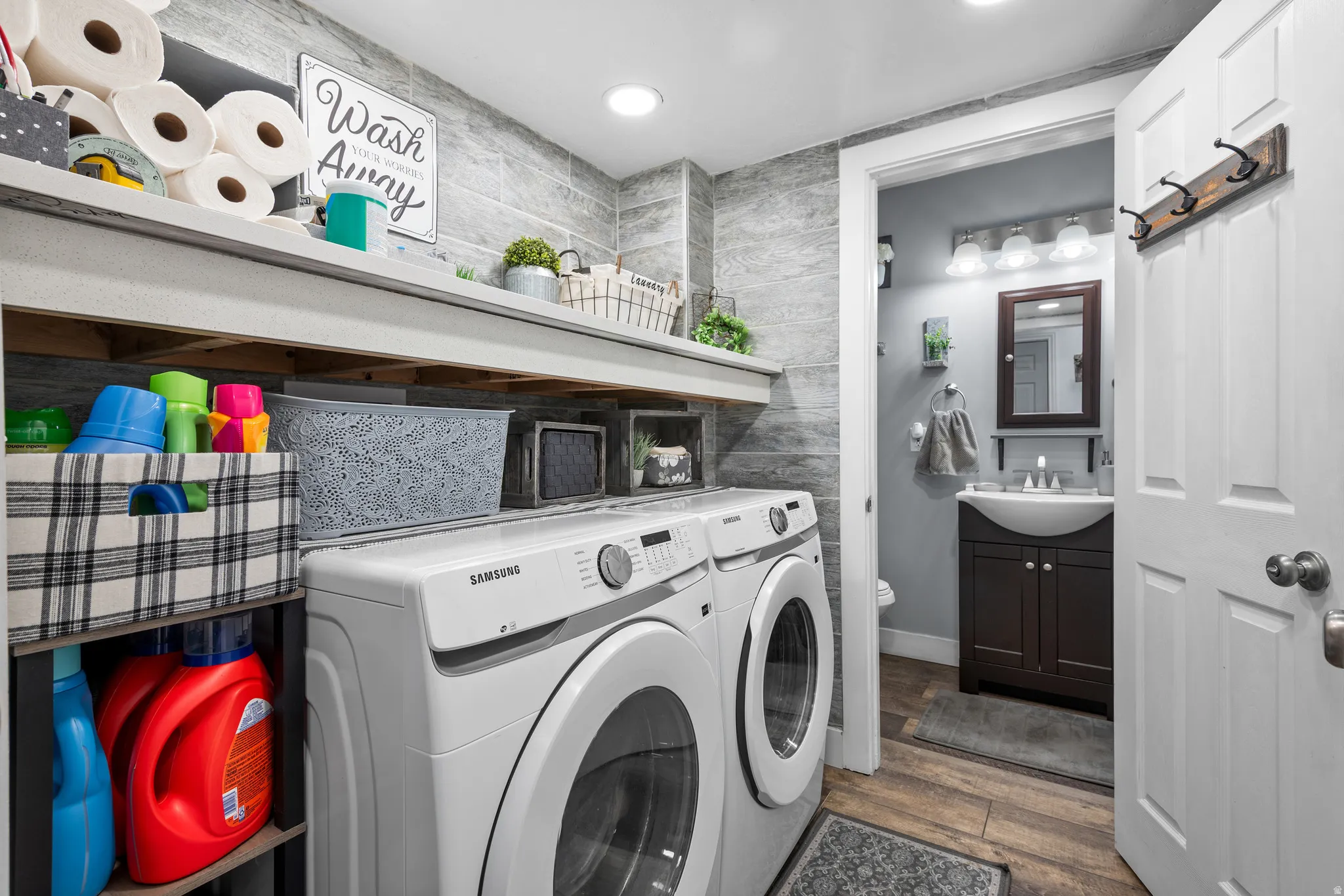 Dedicated laundry space featuring a side-by-side washer and dryer, built-in shelving, and plank-style wall tiling