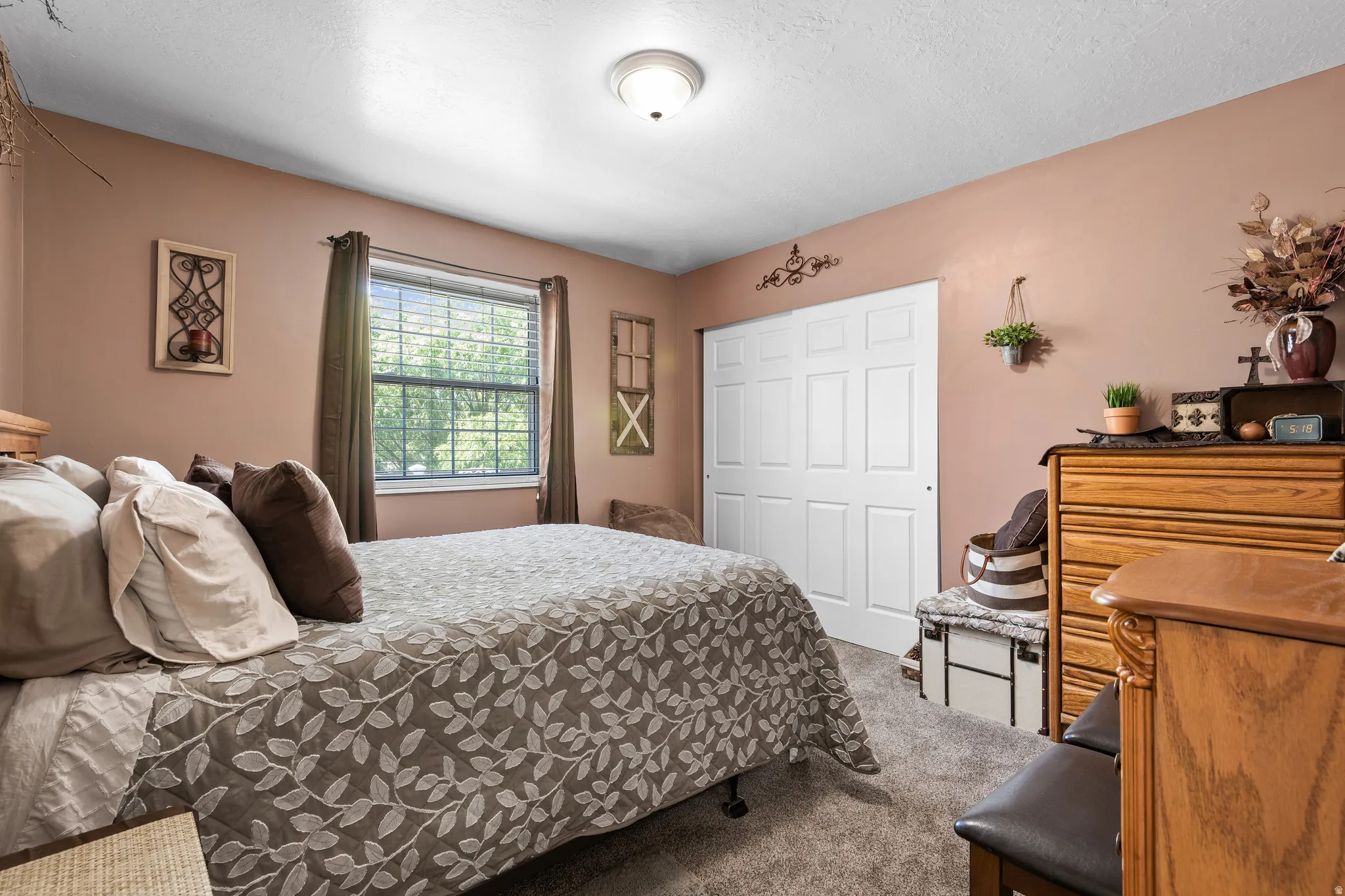 Bedroom featuring a window with natural light, textured carpet flooring, bi-fold closet doors, and a ceiling-mounted light fixture