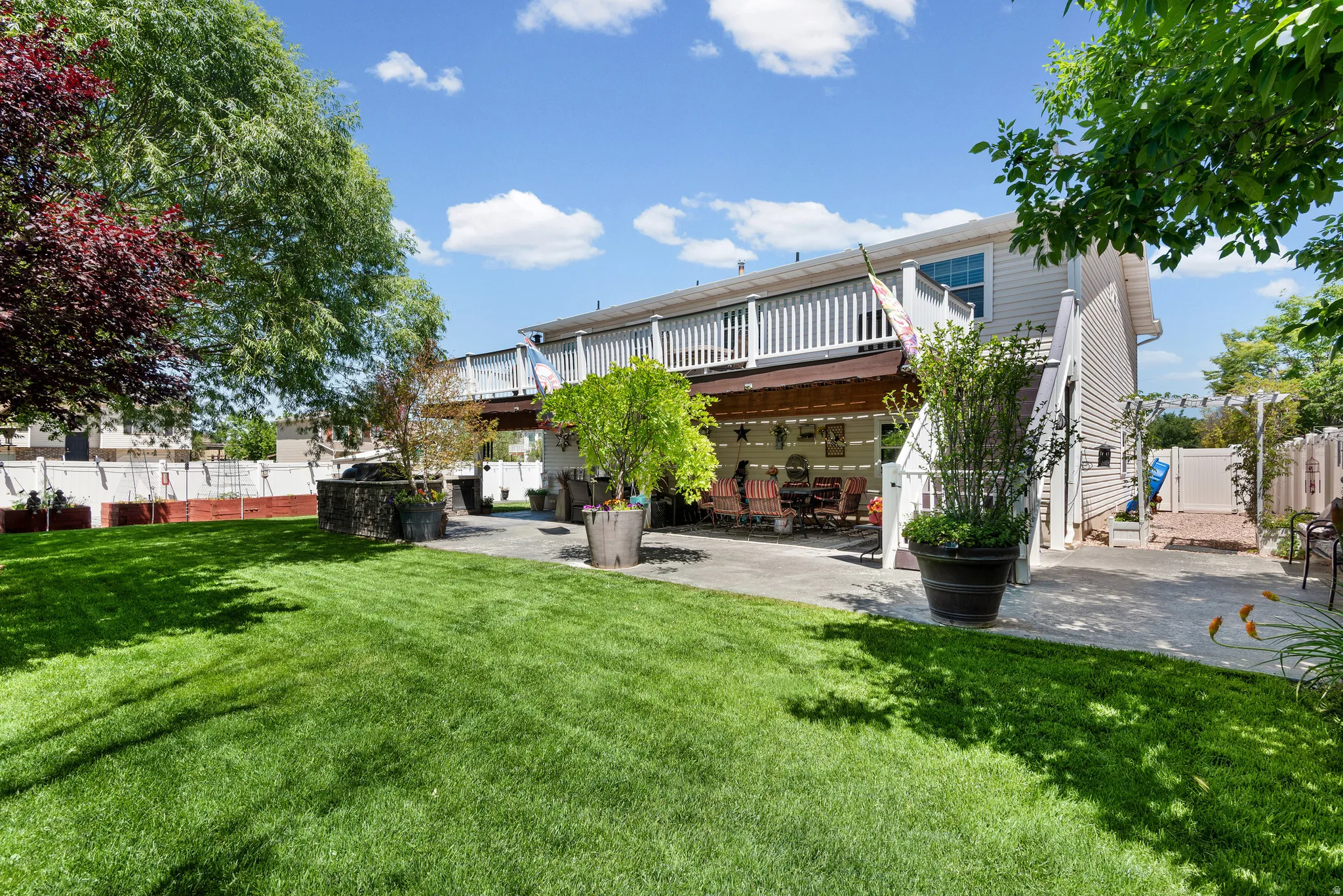 Expansive green lawn with mature trees and a two-story deck featuring white railings