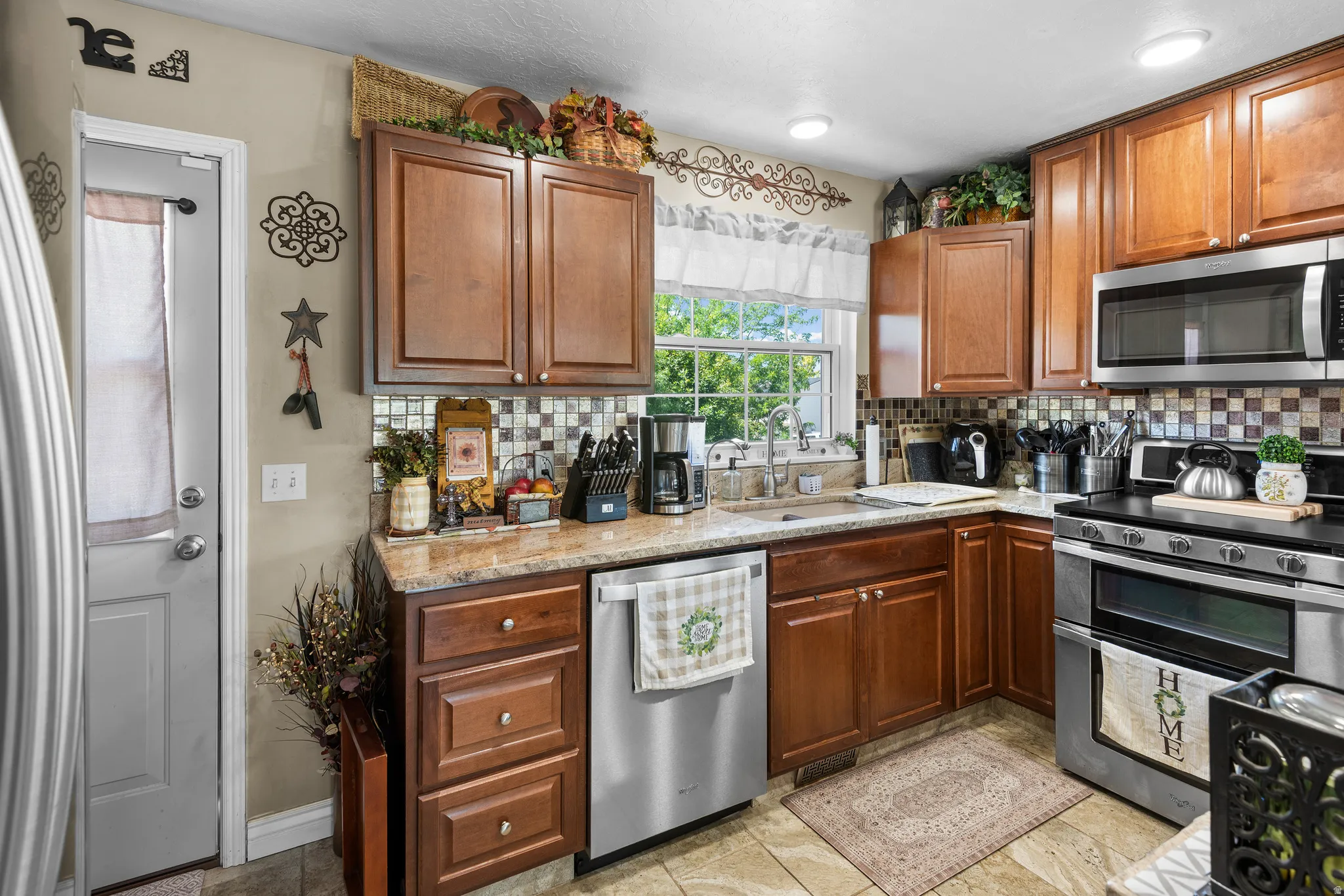Well-appointed kitchen featuring wood cabinetry, granite-style countertops, stainless steel appliances, a mosaic tile backsplash, and recessed lighting