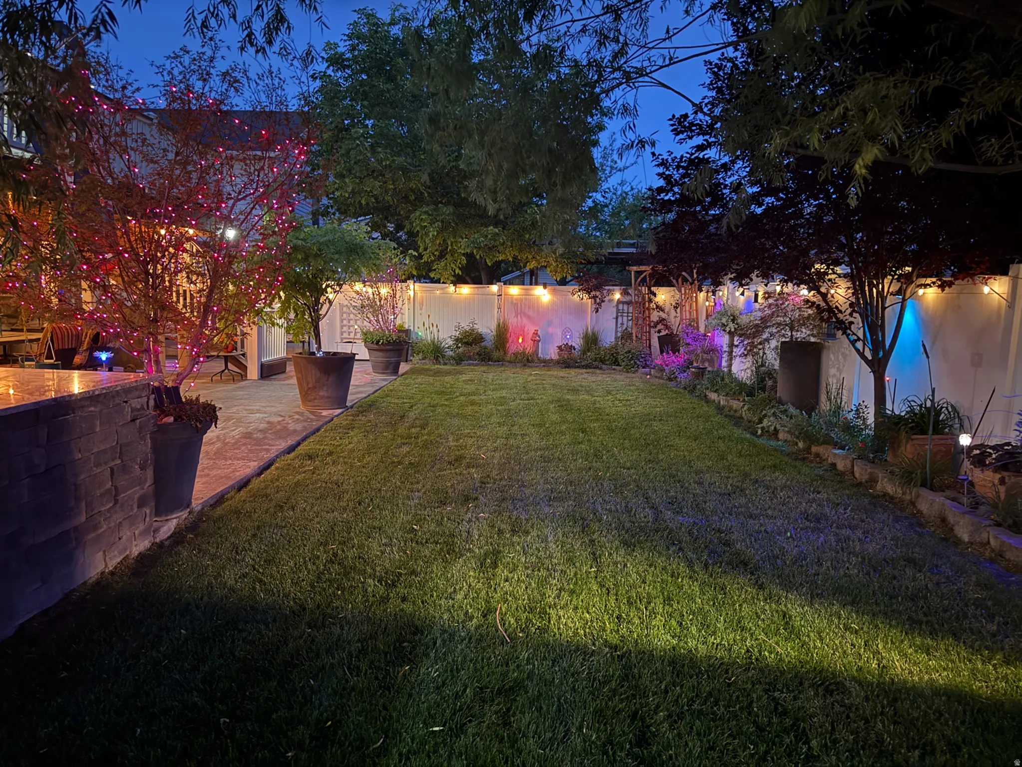 Manicured lawn area bordered by a stone-faced retaining wall and a white privacy fence