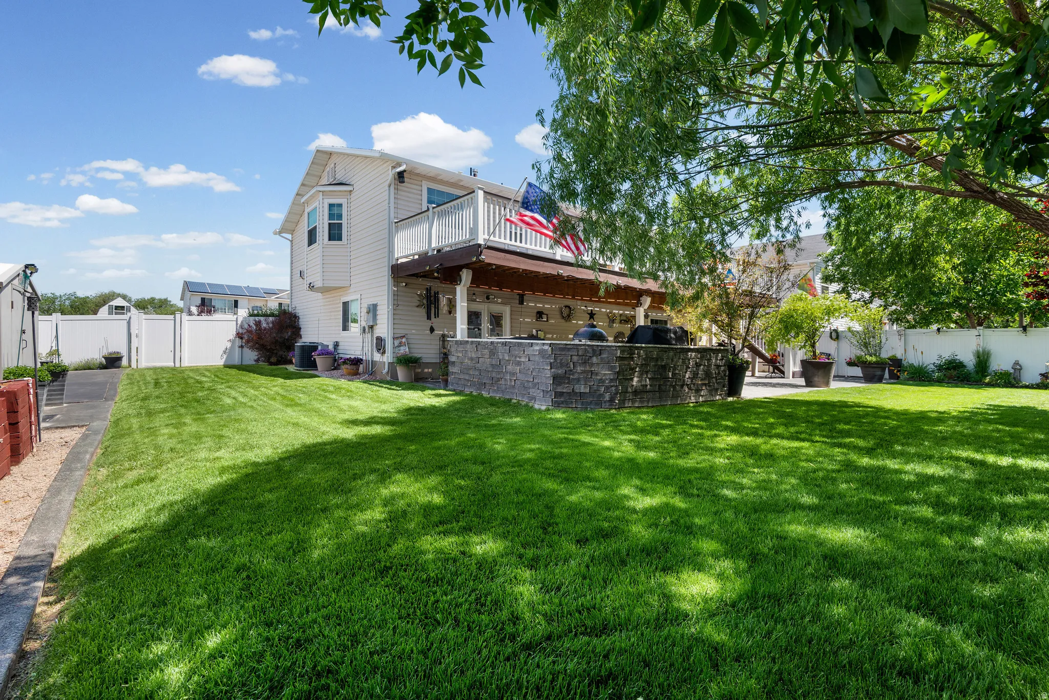 Expansive green lawn featuring a stone-clad outdoor kitchen, a covered patio area, and a second-story balcony