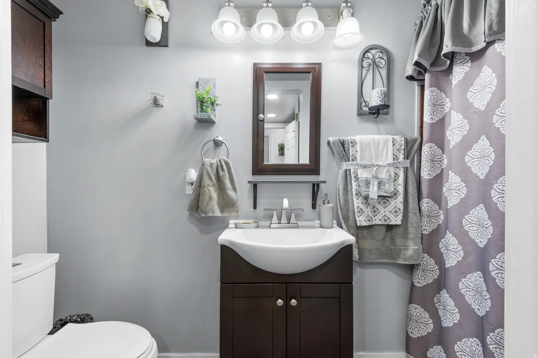 Bathroom featuring a dark wood-finish vanity with a curved vessel sink, chrome faucet, and coordinating dark wood-finish medicine cabinet