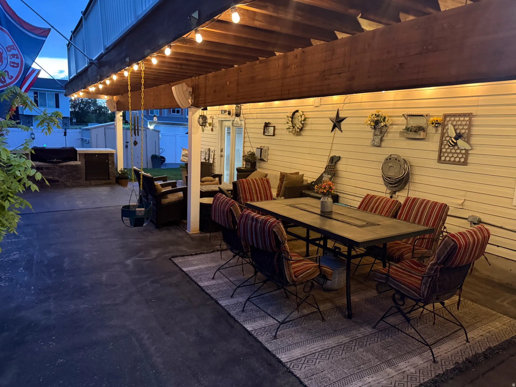 Covered patio featuring exposed wood beams, string lighting, and a built-in outdoor kitchen with stone veneer detailing