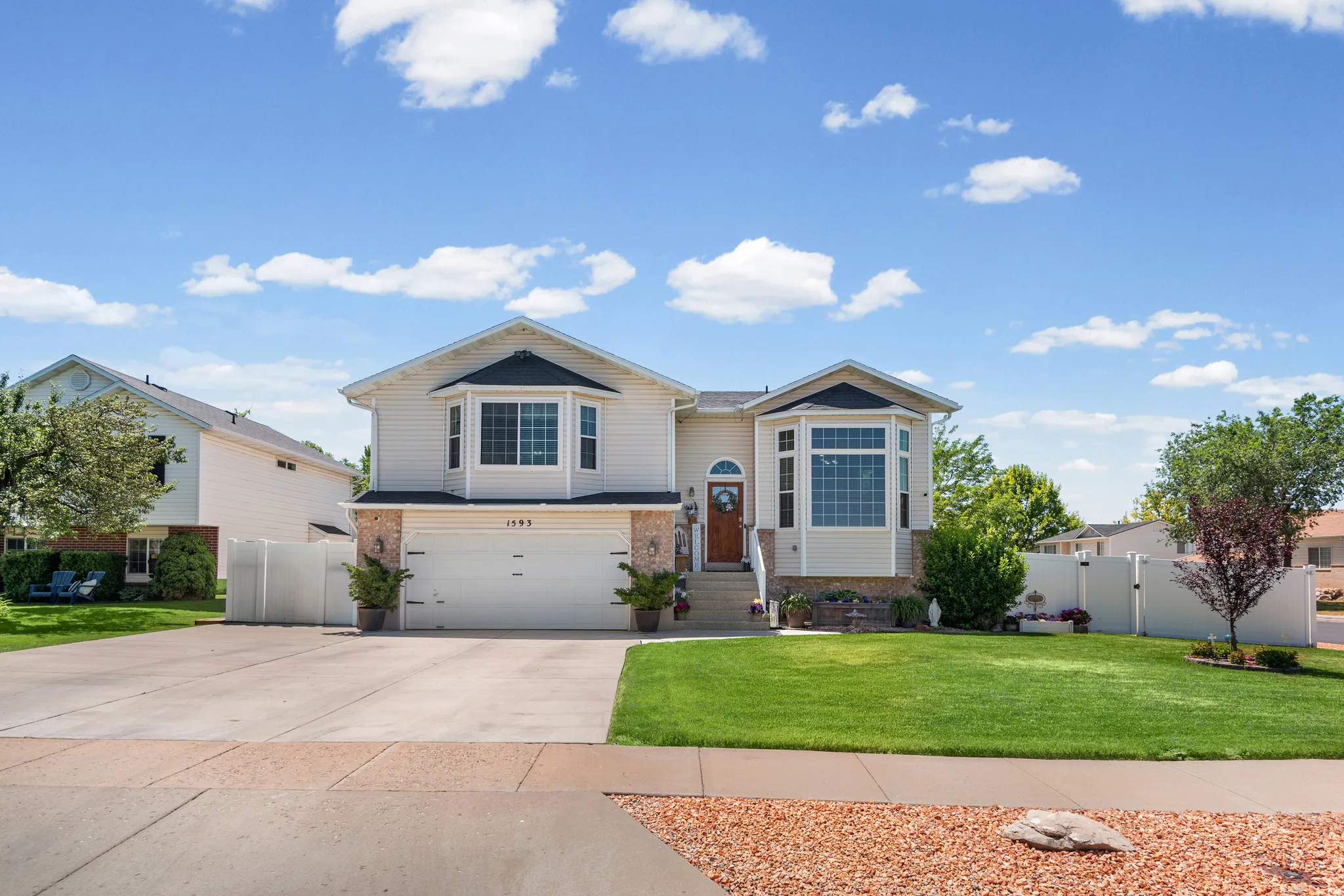 Suburban residence featuring a two-car garage, bay windows, brick accents, a manicured lawn, and a paved driveway