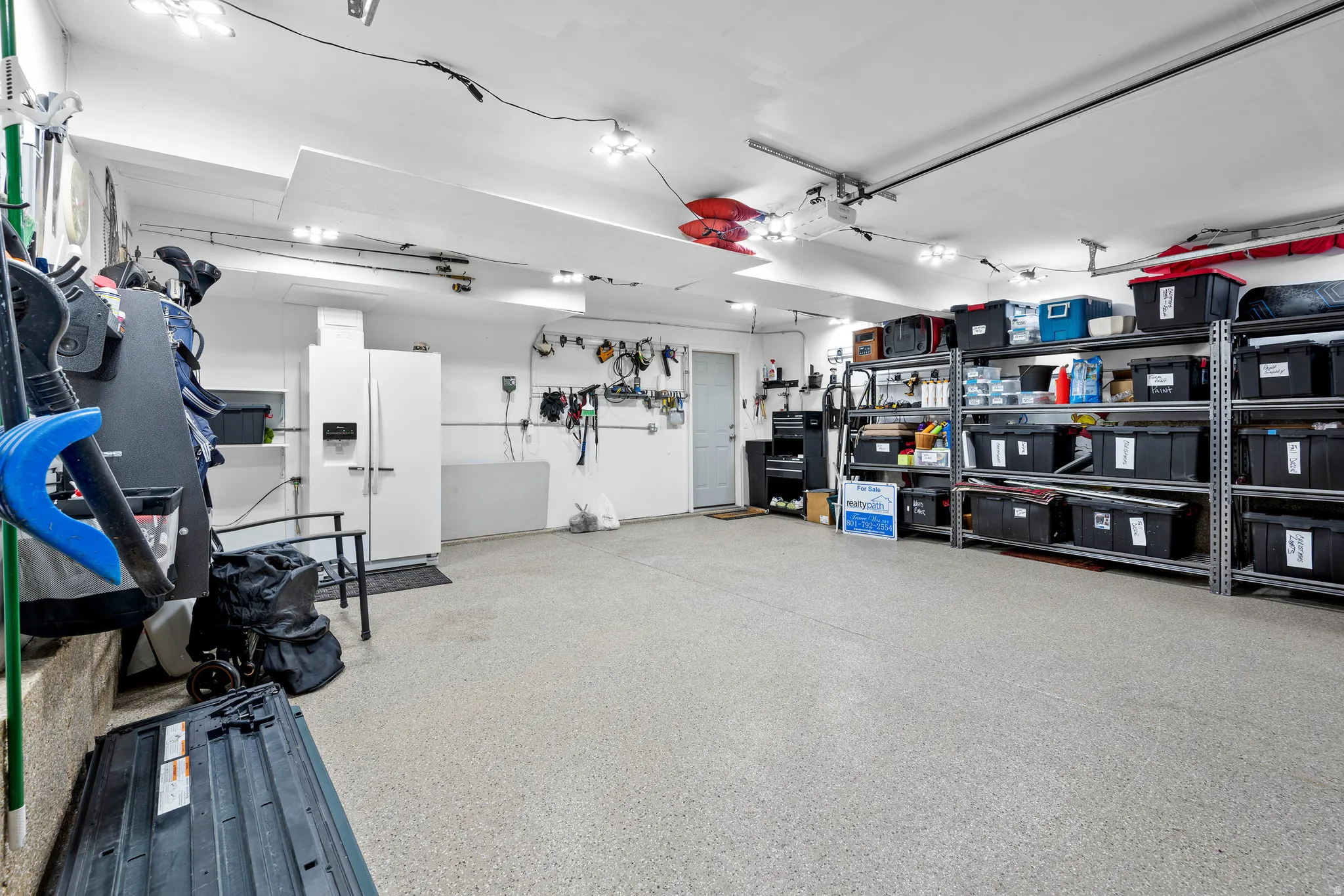 Spacious garage featuring epoxy flooring, extensive built-in shelving, ample overhead lighting, and a side access door