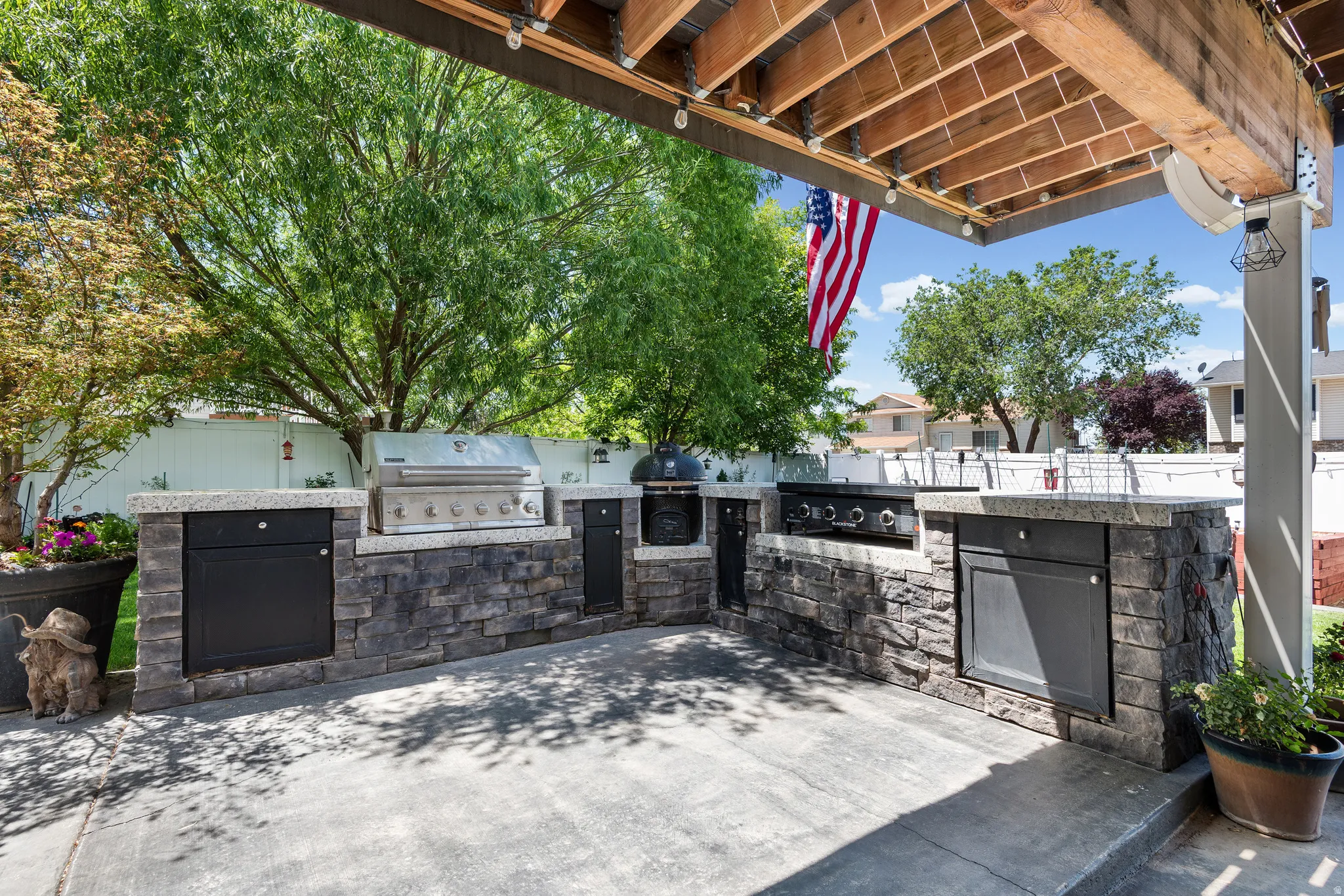 Outdoor kitchen featuring stone veneer base, light-toned countertops, built-in stainless steel grill, and additional cooking elements
