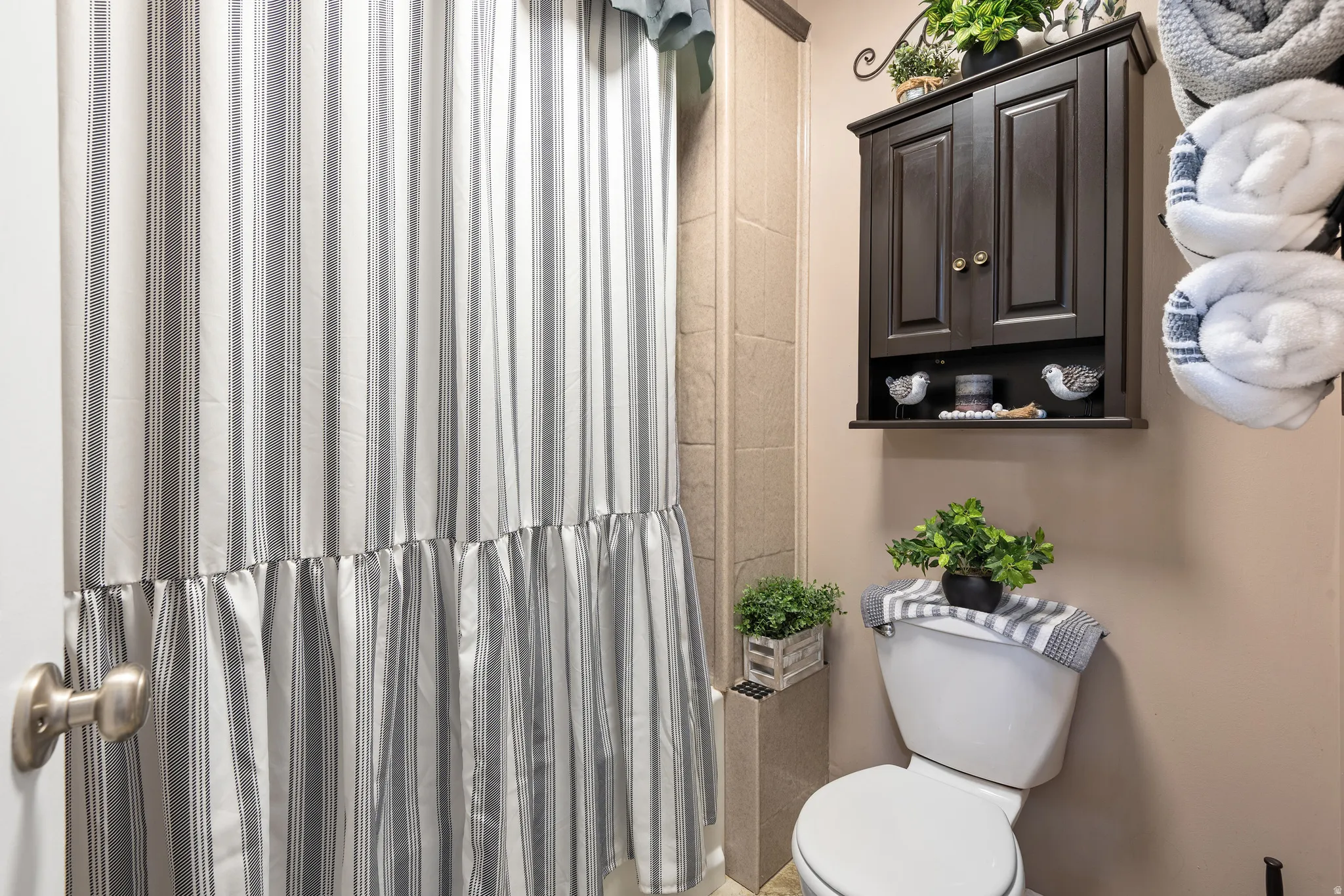 Bathroom featuring a dark wood-finish wall cabinet, a white toilet, and a shower with tile surround