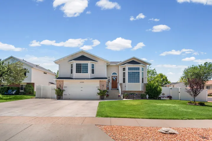 Suburban residence featuring a two-car garage, bay windows, brick accents, a manicured lawn, and a paved driveway