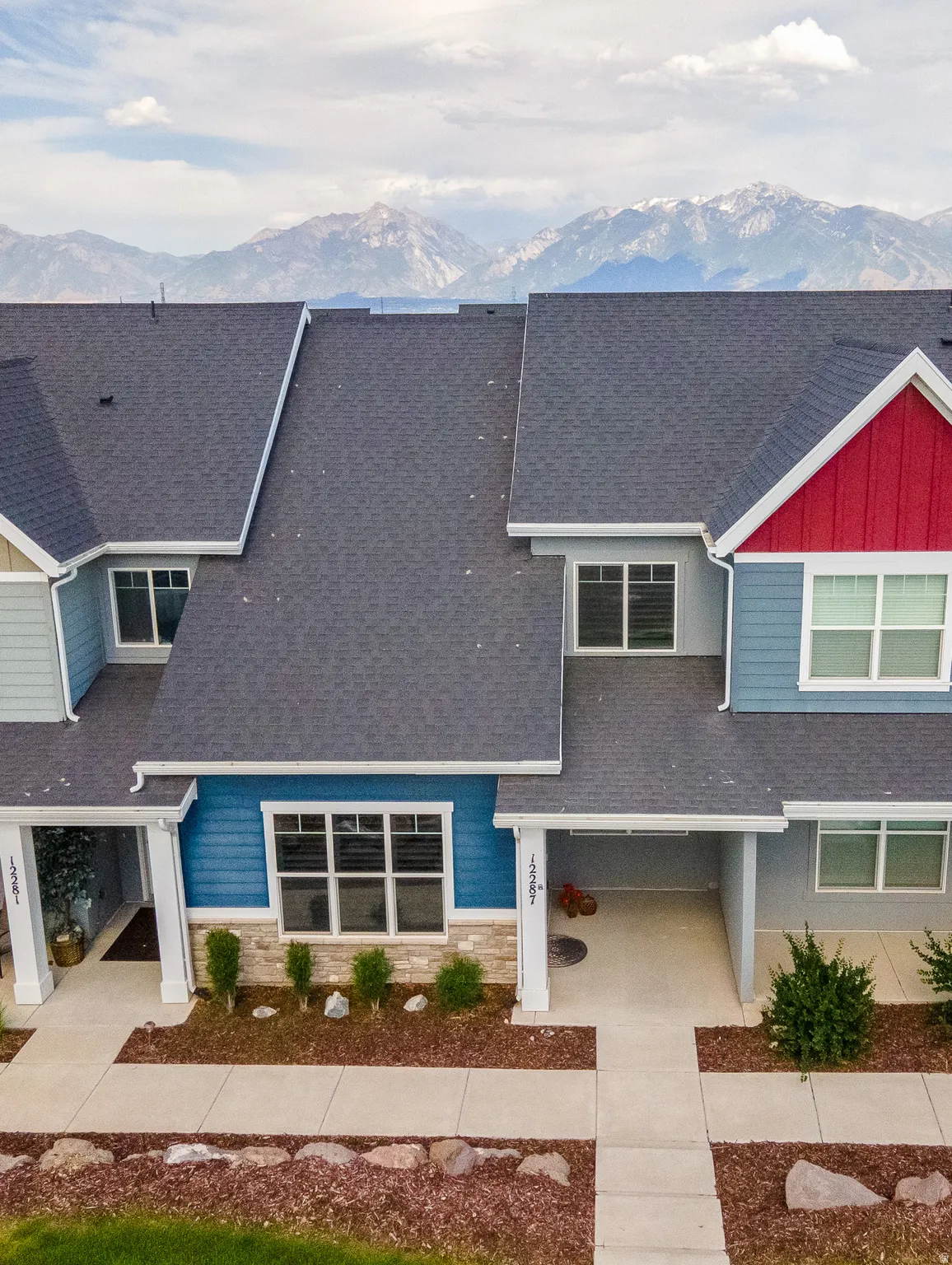 Modern townhome exterior featuring multi-colored siding, a dark shingle roof, and a visible mountain backdrop