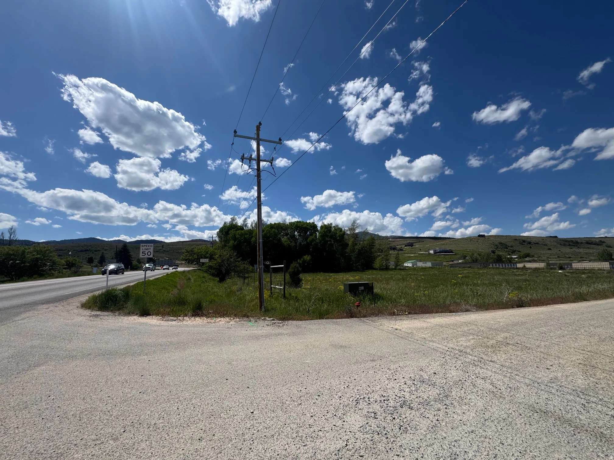 Expansive undeveloped land with a partial paved road frontage and distant hillside backdrop