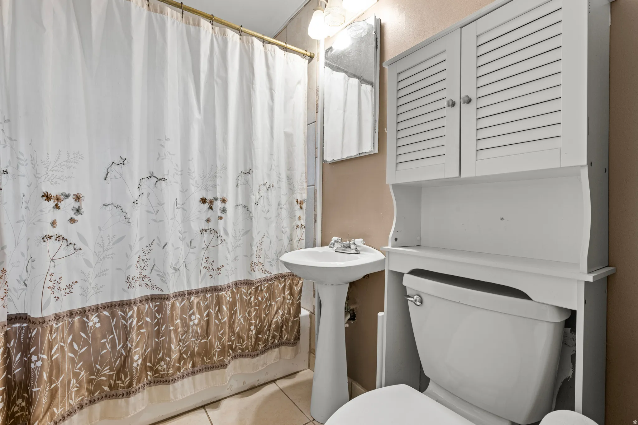 Bathroom featuring a white pedestal sink, toilet, and a white over-the-toilet storage cabinet with louvered doors