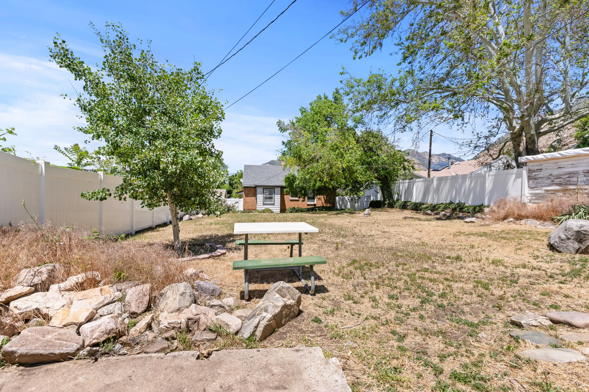 Expansive backyard featuring a privacy fence, mature trees, natural rock landscaping, and a small outbuilding