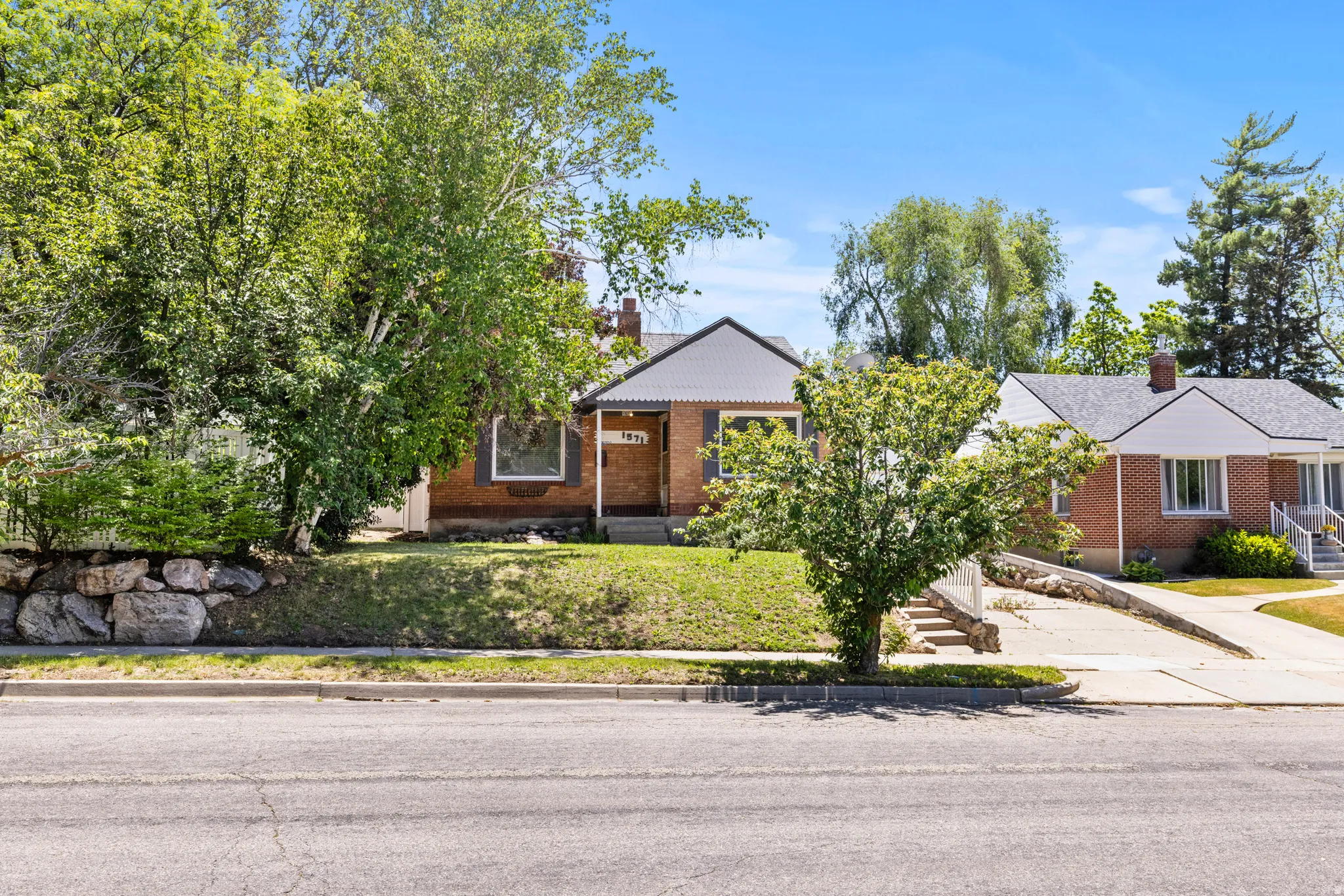 Brick residence with a prominent front lawn, mature trees, and a decorative rock wall