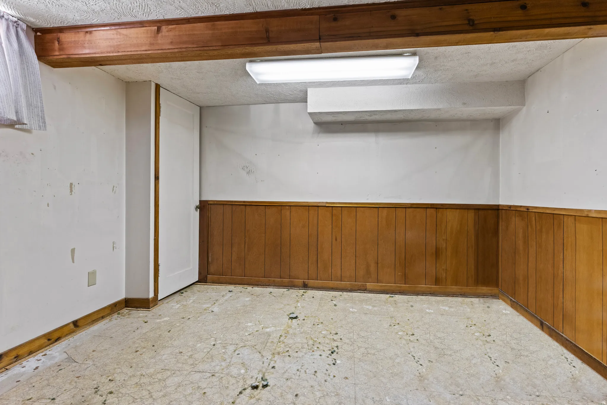 Room featuring wood paneling, white painted walls, exposed wood ceiling beams, and a fluorescent light fixture