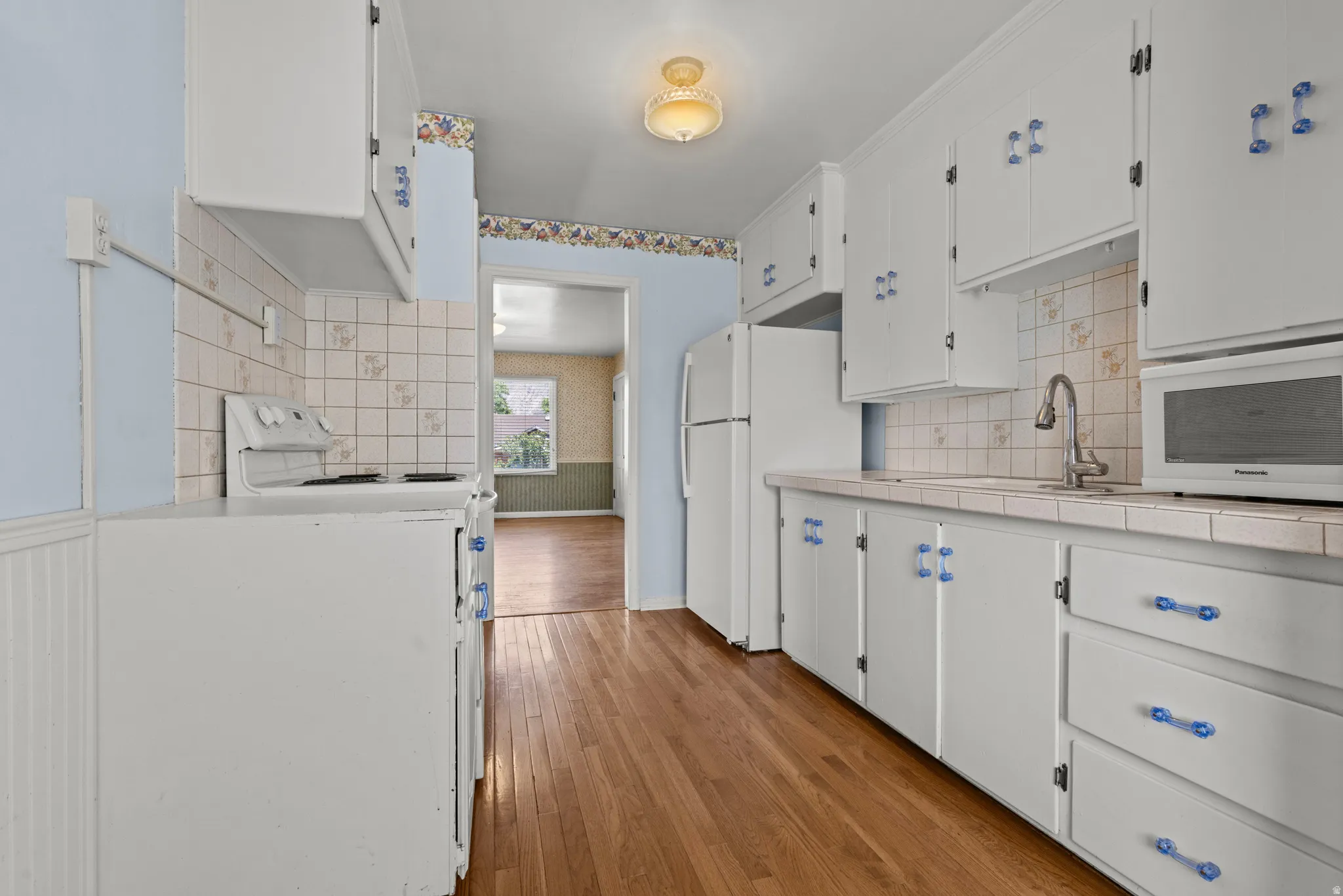 Kitchen featuring wood-finish flooring, white cabinetry with blue hardware, a white refrigerator, and a white range